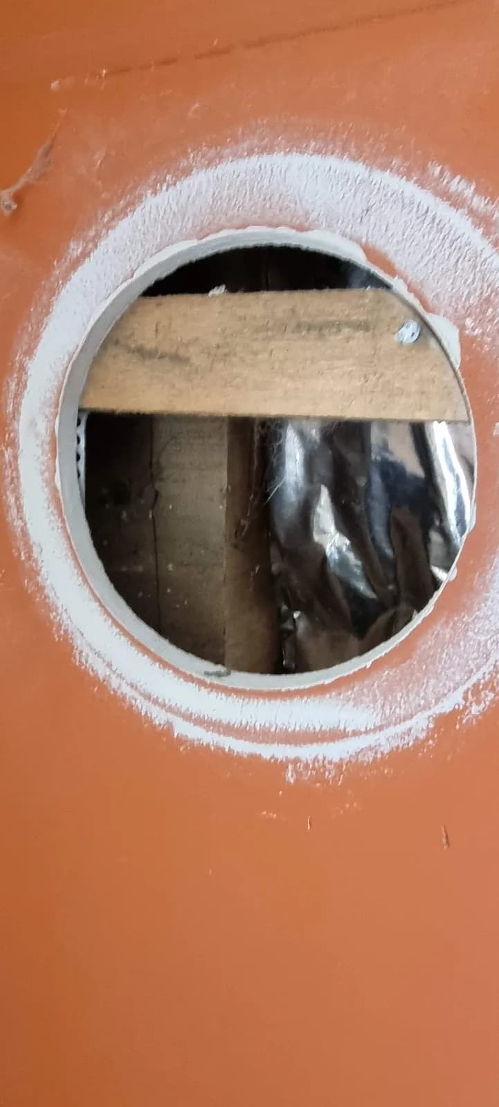 Kör alakú nyílás a falburkolaton, mögötte látható fa szerkezettel